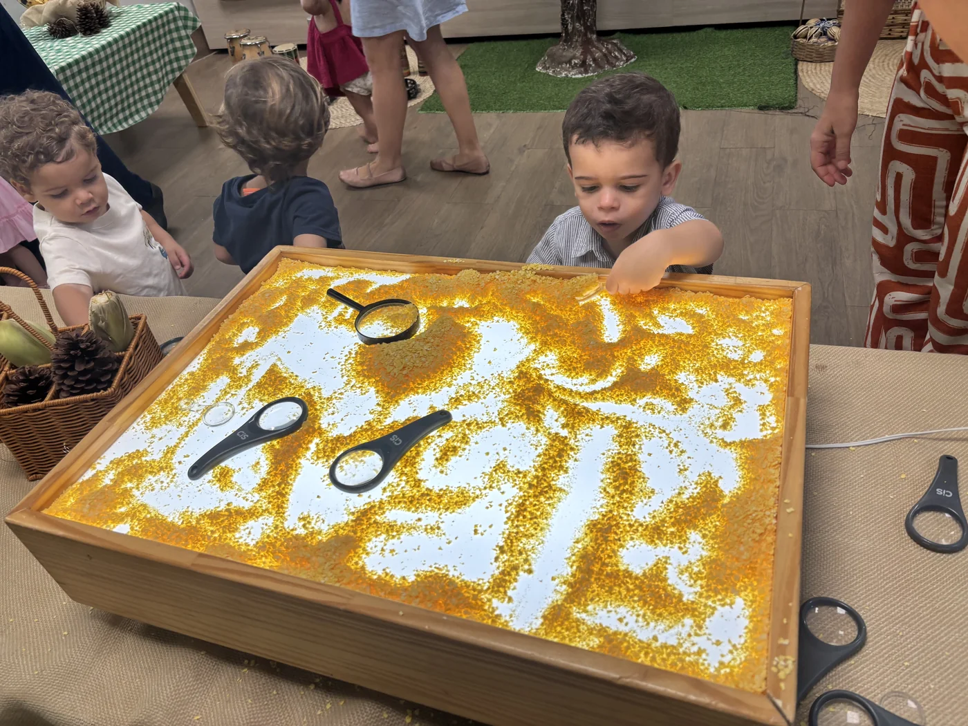 Bebê explorando caixa sensorial luminosa com grãos