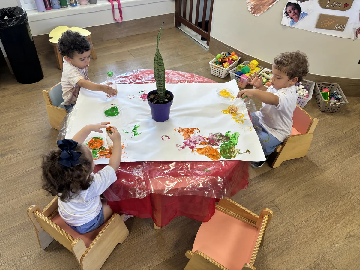 Três crianças pintando em mesinhas individuais